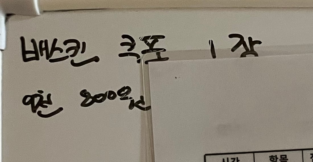 화이트보드 왼쪽 면의 손글씨 확대. 검은 보드마카로 두 줄이 적혀 있다. 윗줄은 '배스킨 쿠폰 1장', 아랫줄은 '9천800원'.